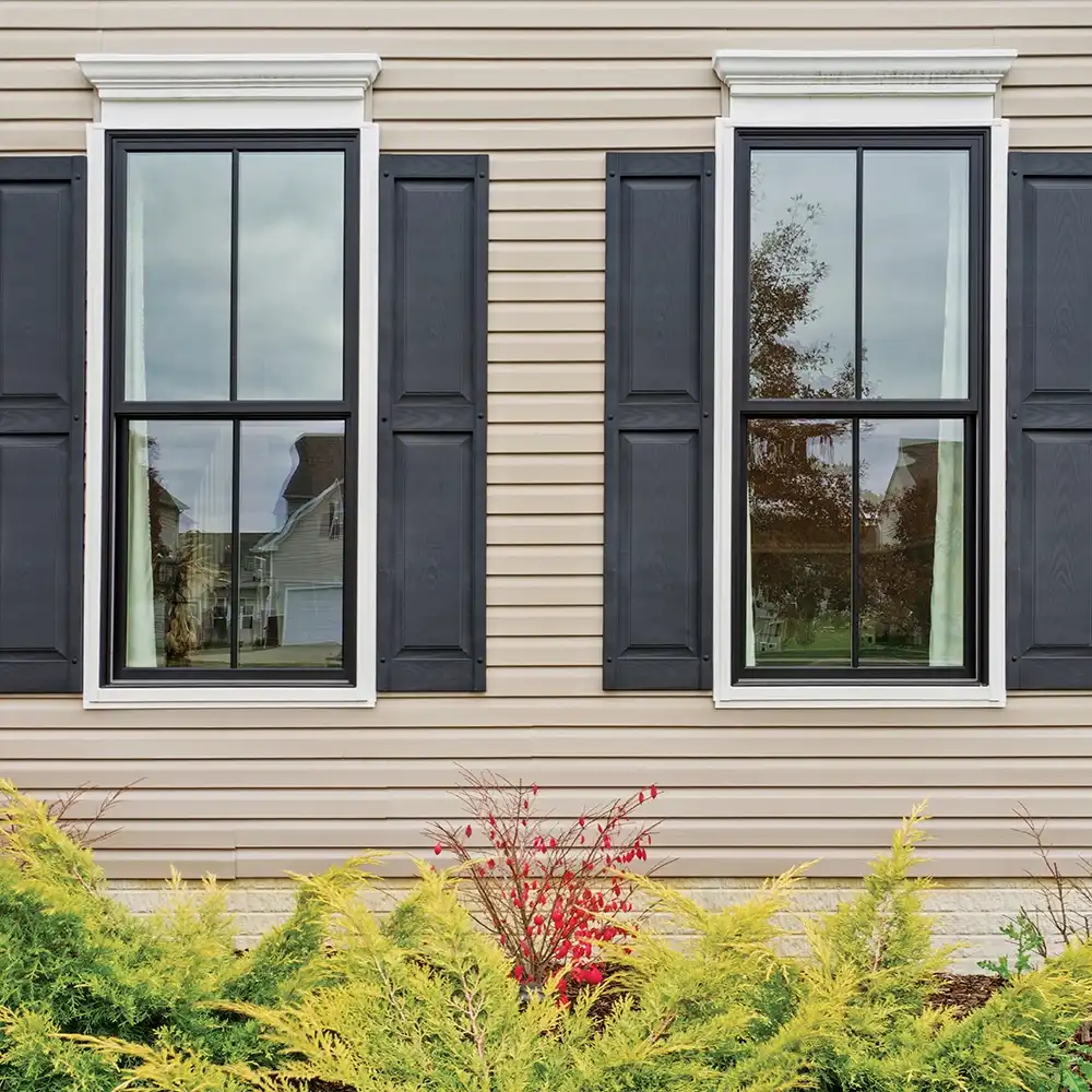 Exterior view of black Marvin Replacement single hung windows with grilles and shutters.