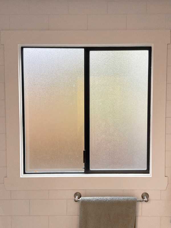 Interior view of a black slider window in a bathroom with privacy glass.