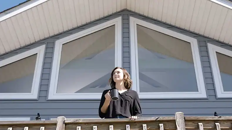 Woman drinking coffee on a wood deck featuring Marvin Replacement Polygon Windows.
