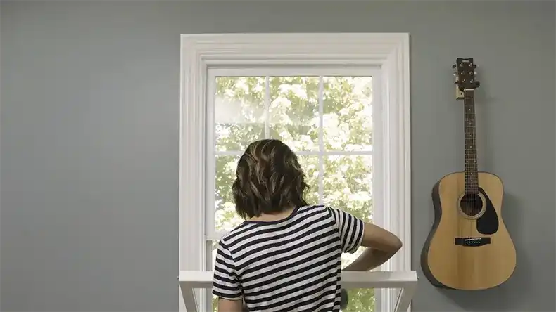 Woman in striped shirt cleans a white double hung Marvin Replacement window
