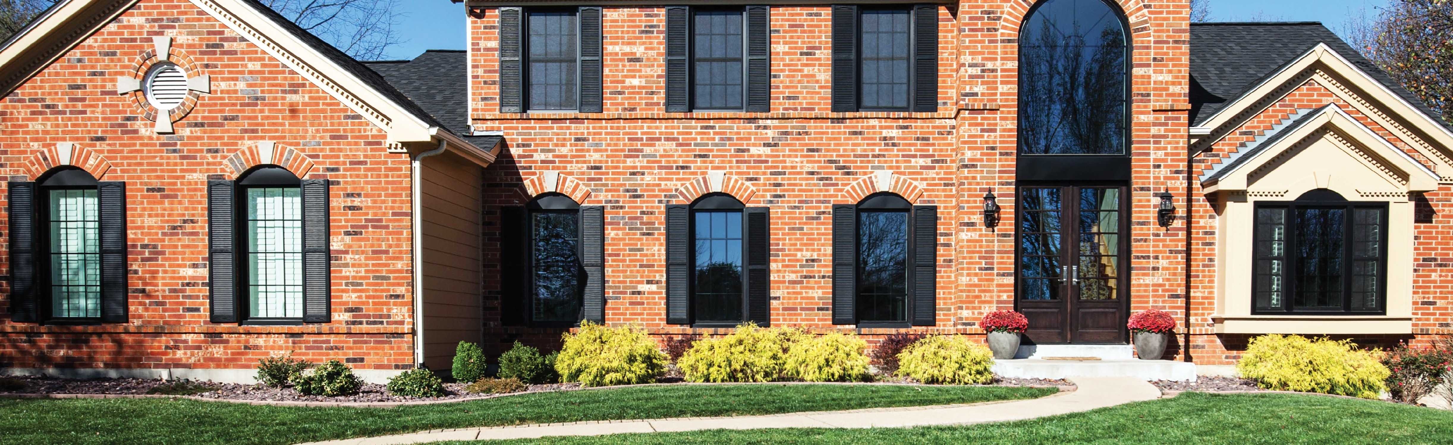 Exterior view of Marvin Replacement black Single Hung windows on a brick house with black shutters.