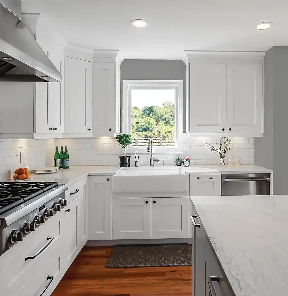 Interior view of a white kitchen with a Marvin Replacement picture window above a farmhouse sink.