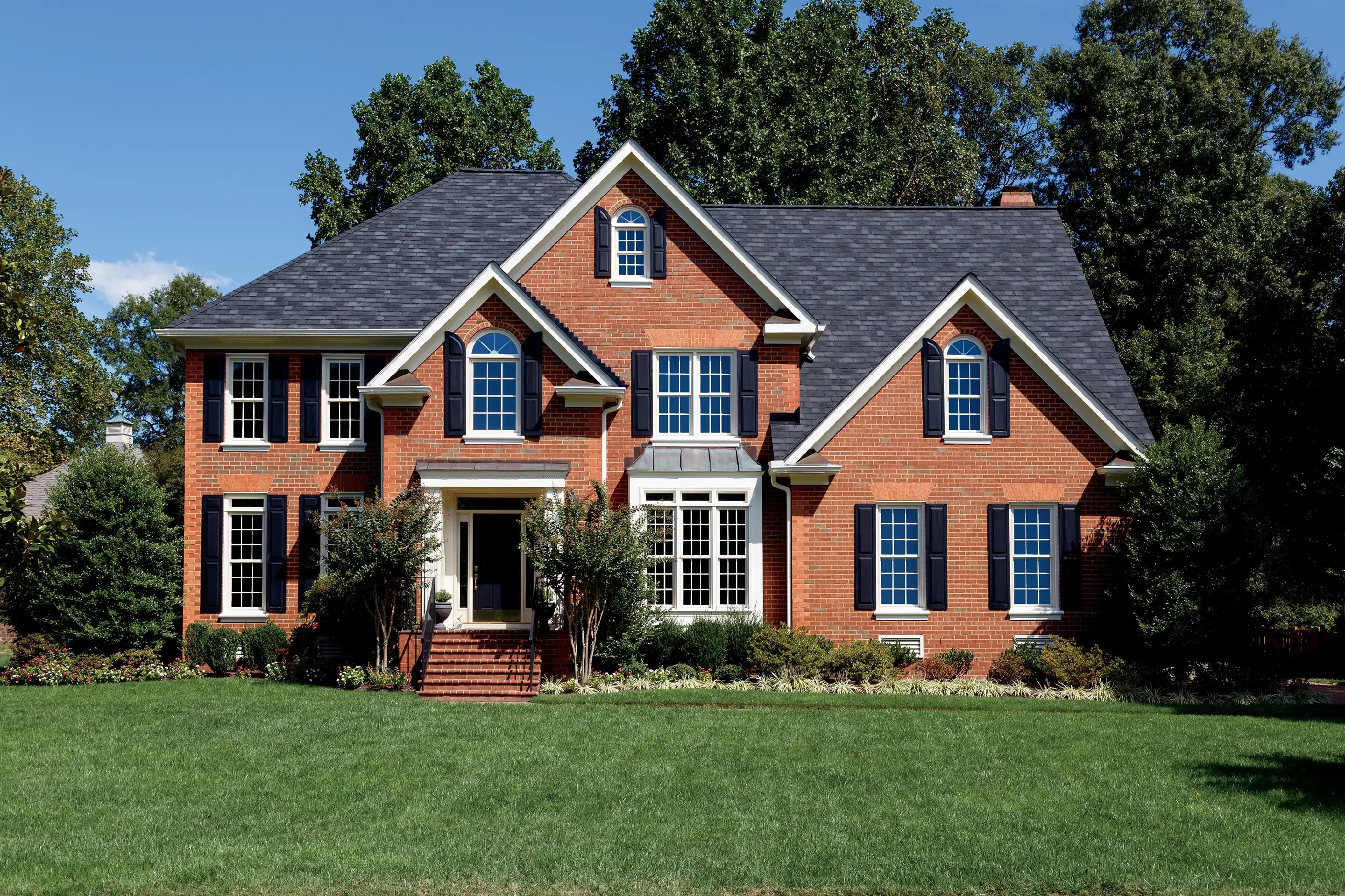 Exterior view of a brick home featuring white Marvin Replacement windows and black shutters.