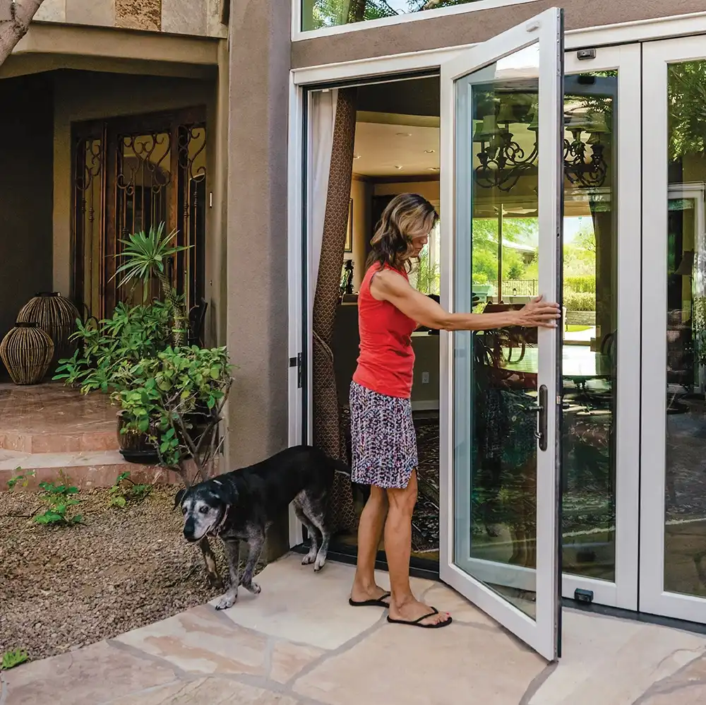 A woman opens a Marvin Replacement bi-fold patio door as a dog walks out.