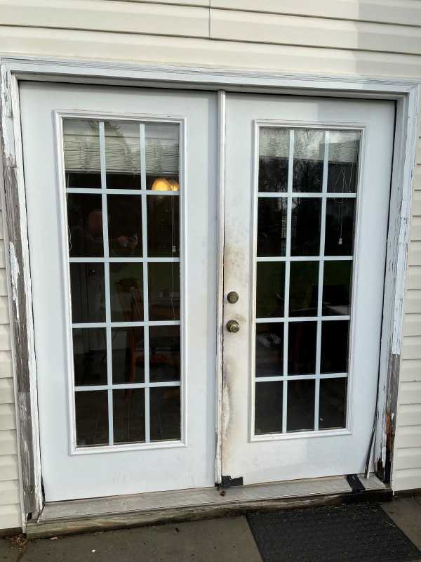 Exterior view of a damaged, old white French door on a patio.