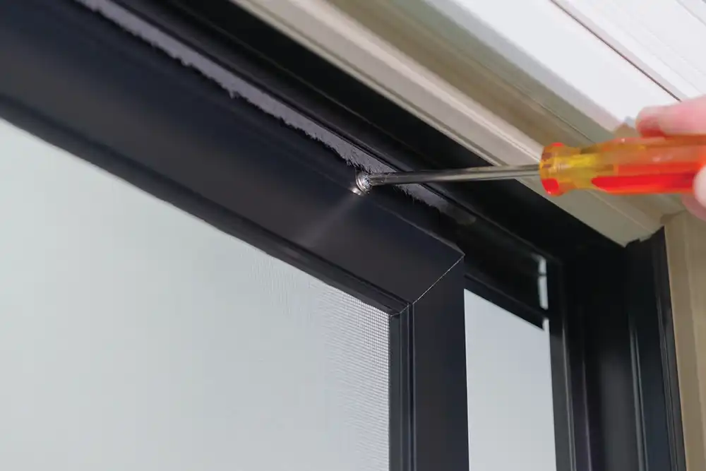 A screwdriver tightens a screw on a Marvin Replacement patio door screen.