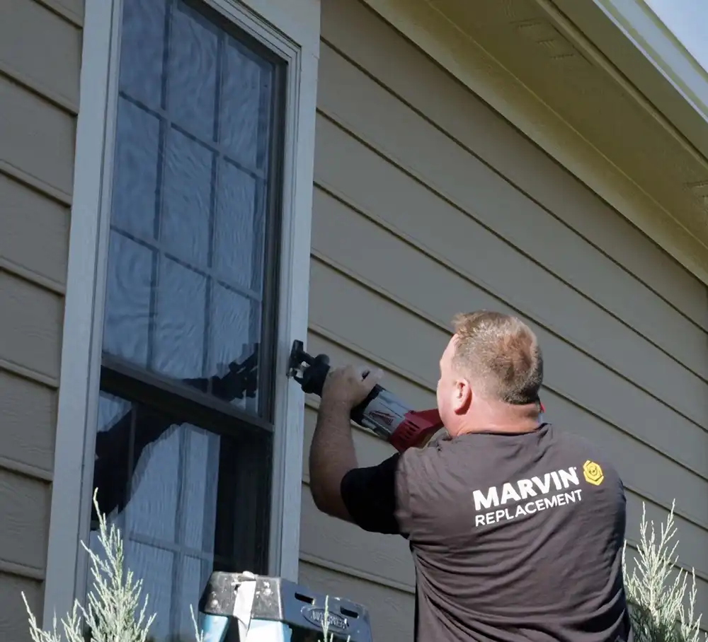 A Marvin Replacement installer uses a reciprocating saw to remove an old window outside a home.