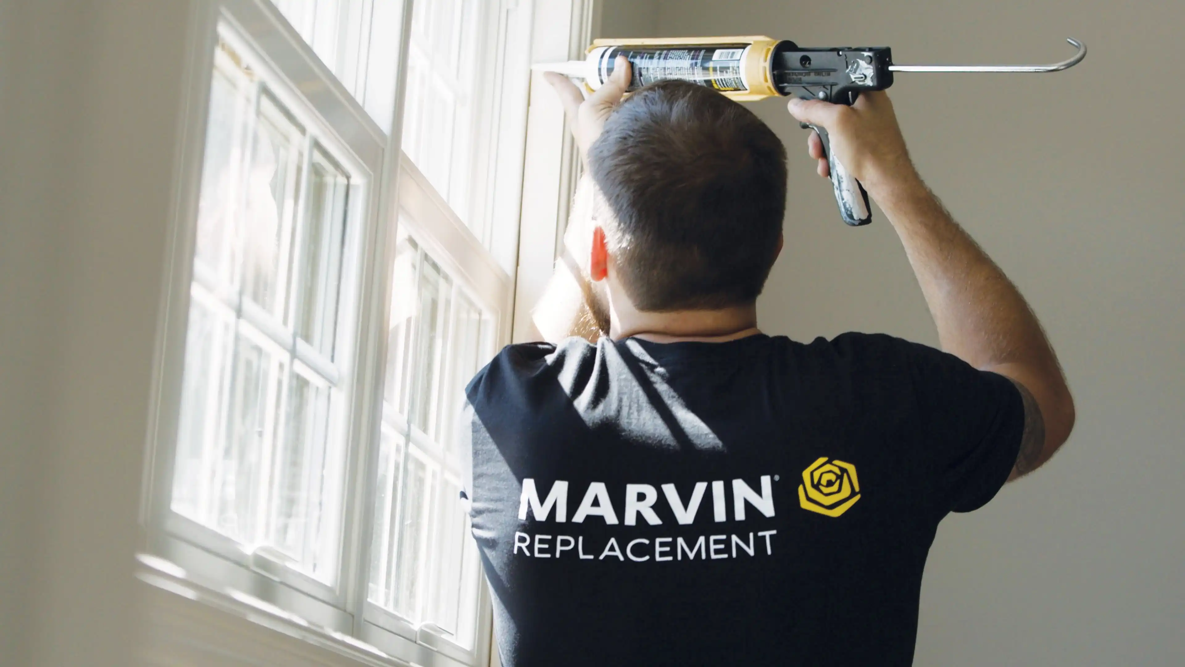 A Marvin Replacement window installers uses a caulk gun to seal a window. 