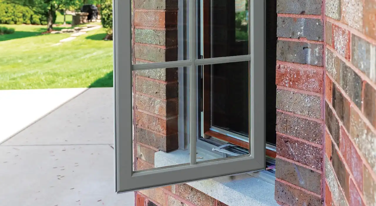 Exterior view of an opened brown casement window with grids on a brick home.