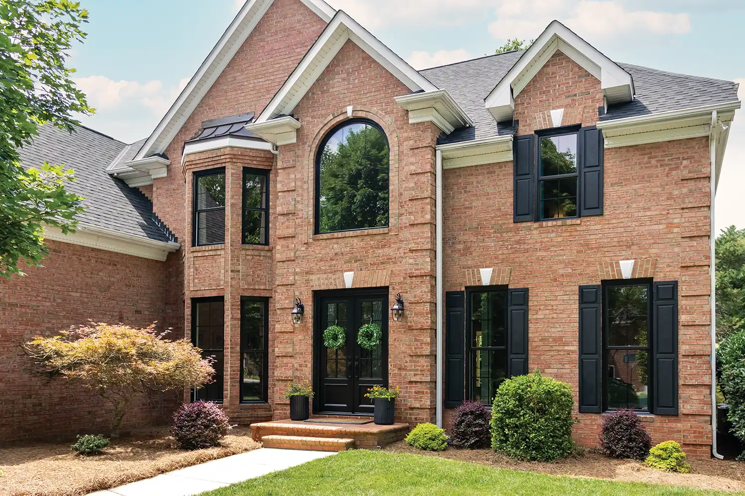 Exterior view of a brick home with black windows and black shutters.